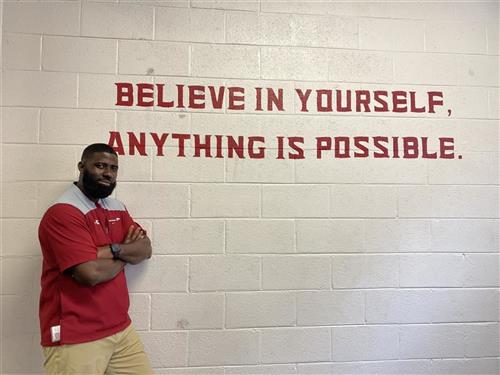  Cedric Tyson poses in front of a wall that reads "Believe in Yourself, Anything is possible."